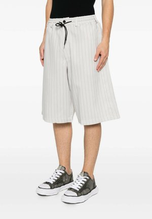 Man draagt witte shorts met smalle strepen en een zwart trekkoord, gecombineerd met zwart-witte vetersneakers.