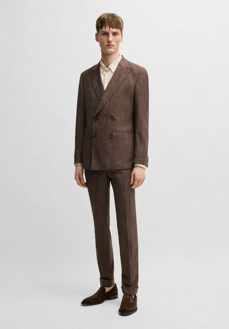 Costume marron texturé à double boutonnage avec revers crantés, associé à une chemise de couleur claire et des chaussures en croûte de cuir marron. Pantalon slim fit.