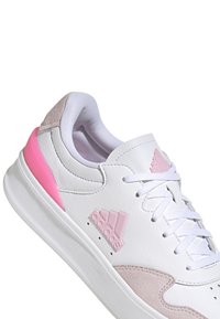 Sneaker sportivo bianco con dettagli rosa, realizzato in pelle e camoscio. Presenta una suola testurizzata e il classico logo a tre strisce di lato.