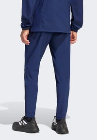 Granatowe spodnie sportowe o zwężanym kroju, wykonane z lekkiego materiału, z zasuwanymi na suwak bocznymi szwami, zestawione z czarnymi butami sportowymi z białymi akcentami.