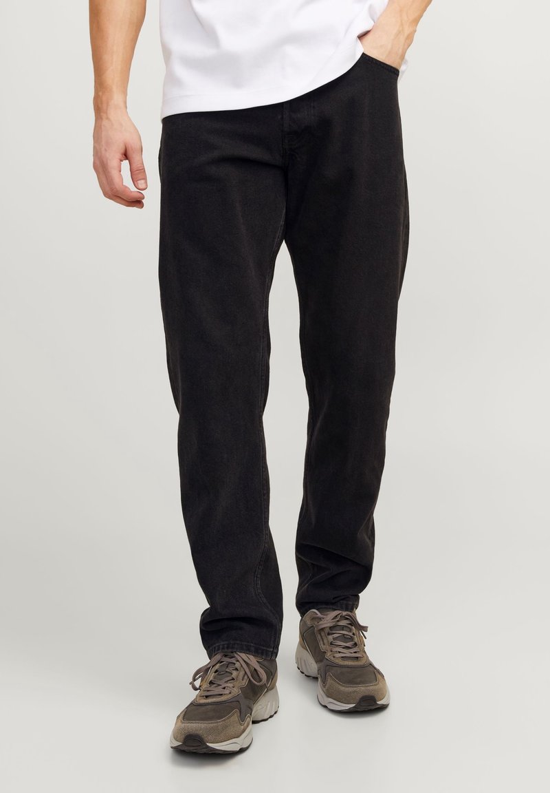 Svarta bomullsh/byxor med avslappnad passform, utrustade med bälteshällor och sidofickor, kombinerade med grå sneakers och en vit t-shirt.