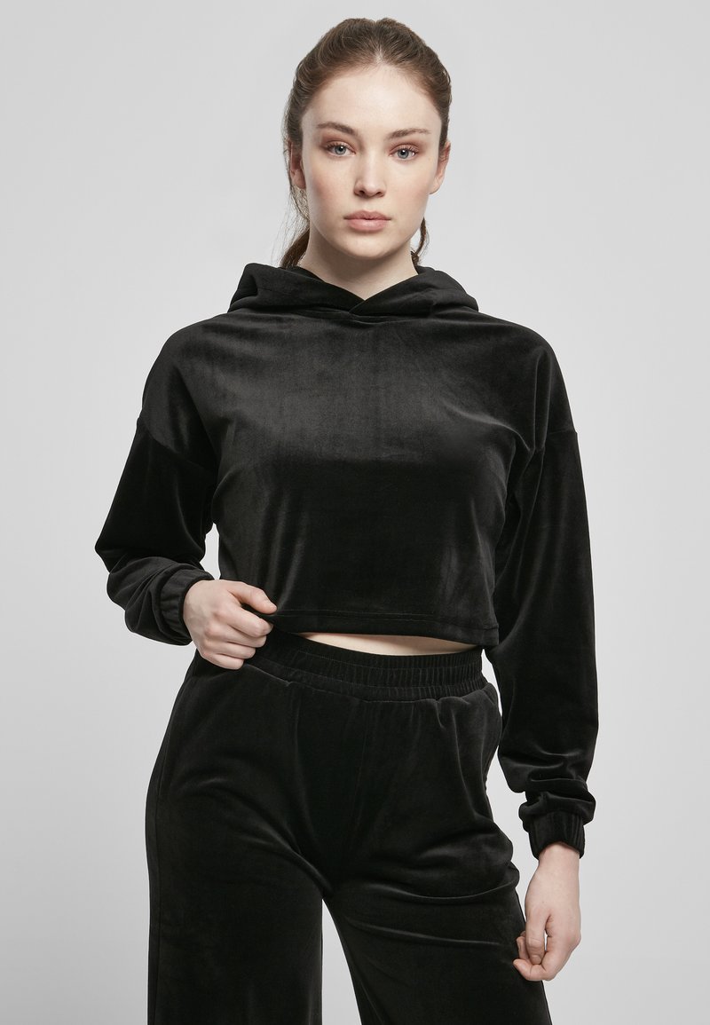 Svart cropped hoodie laget av myk velvet med en frontlomme. Lange ermer med ribbestrikkede mansjetter, sammen med matchende velvet joggebukser.