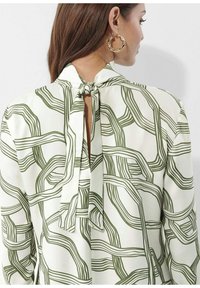 Weißes Blusenshirt mit grünem abstraktem Linienmuster, mit gebundenem Ausschnitt auf der Rückseite, offenen Ausschnitten, langen Ärmeln und glatter Textur.