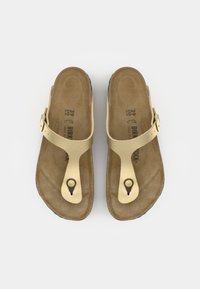 Goldfarbene Sandalen mit flacher Sohle, verstellbarem Riemen und Zehensteg. Die Fußbett ist strukturiert und zeigt Größenangaben sowie das Markenlogo.