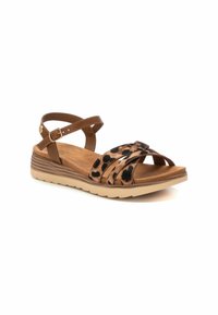 Sandal con estampado de leopardo en tonos marrón y negro, con tiras cruzadas, hebilla en el tobillo y suela texturizada de color marrón claro. Diseño plano con un leve tacón.