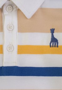 Polo a righe in cotone. Presenta righe color beige chiaro, bianco, giallo e blu, tre bottoni e un ricamo di giraffa blu.