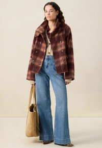 Veste en laine à carreaux marron avec de grands boutons, gilet beige en dessous, jeans évasés en denim bleu taille haute et sac fourre-tout en daim beige.