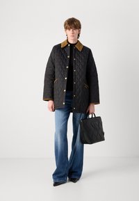 Quilted black jacket with brown collar, gold hardware, and side pockets, paired with flared blue jeans and a black textured handbag.