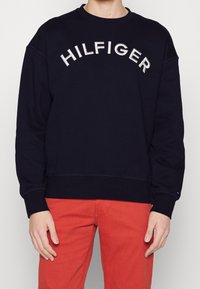 Sudadera azul marino de algodón, con un gran logo bordado en blanco que dice "HILFIGER" en el pecho y puños y dobladillo acanalados.