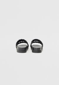 Svart slide-sandaler med doble flettede stropper, flat såle og glatt tekstur. Minimalistisk design med en enkel, moderne silhuett.