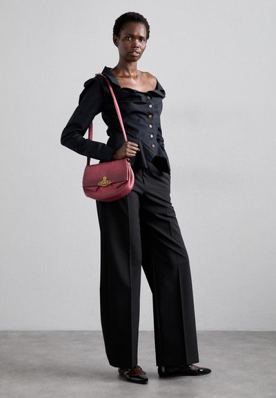 Blusa preta de botão com design de ombro a descoberto, combinada com calças largas pretas. Bolsa rosa de ombro com detalhe em emblema dourado.