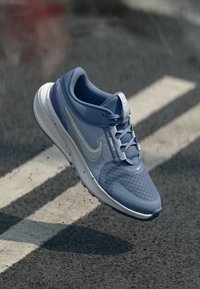 Svijetloplave atletske tenisice s teksturiranim mrežastim gornjim dijelom, istaknutim bijelim logotipom u obliku swoosh, udobnom potplatom i sivim akcentima.