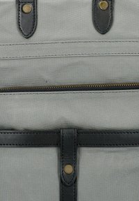 Borsa in tela grigia con accenti in pelle nera, hardware in ottone, tasca con cerniera e un design snodato e piatto con dettagli di cucitura.