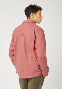 Roze, gestructureerde shirt met een puntige kraag, enkele rugnaad en knoopdetails op de manchetten, gedragen met olijfgroene broek.
