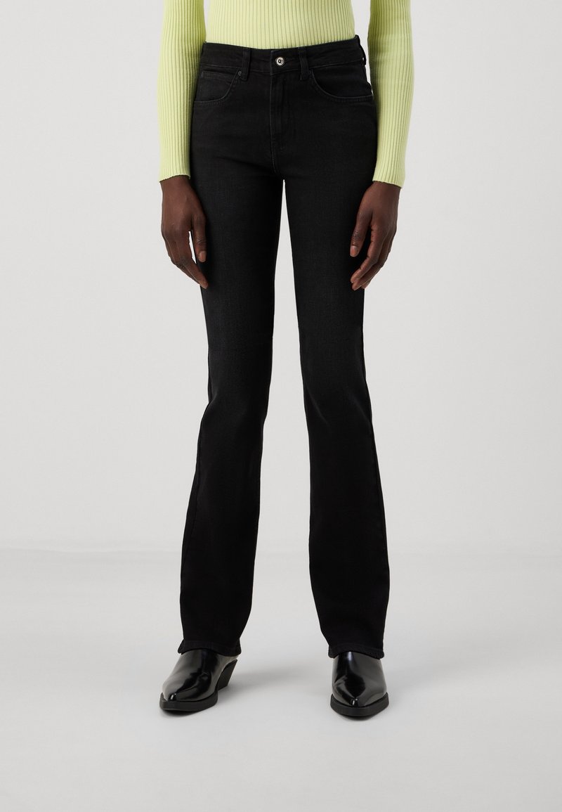 Vaqueros de mezclilla negros de campana con una textura suave. Presentan un diseño clásico de cinco bolsillos y una cintura ajustada, combinados con una blusa de canalé verde brillante.