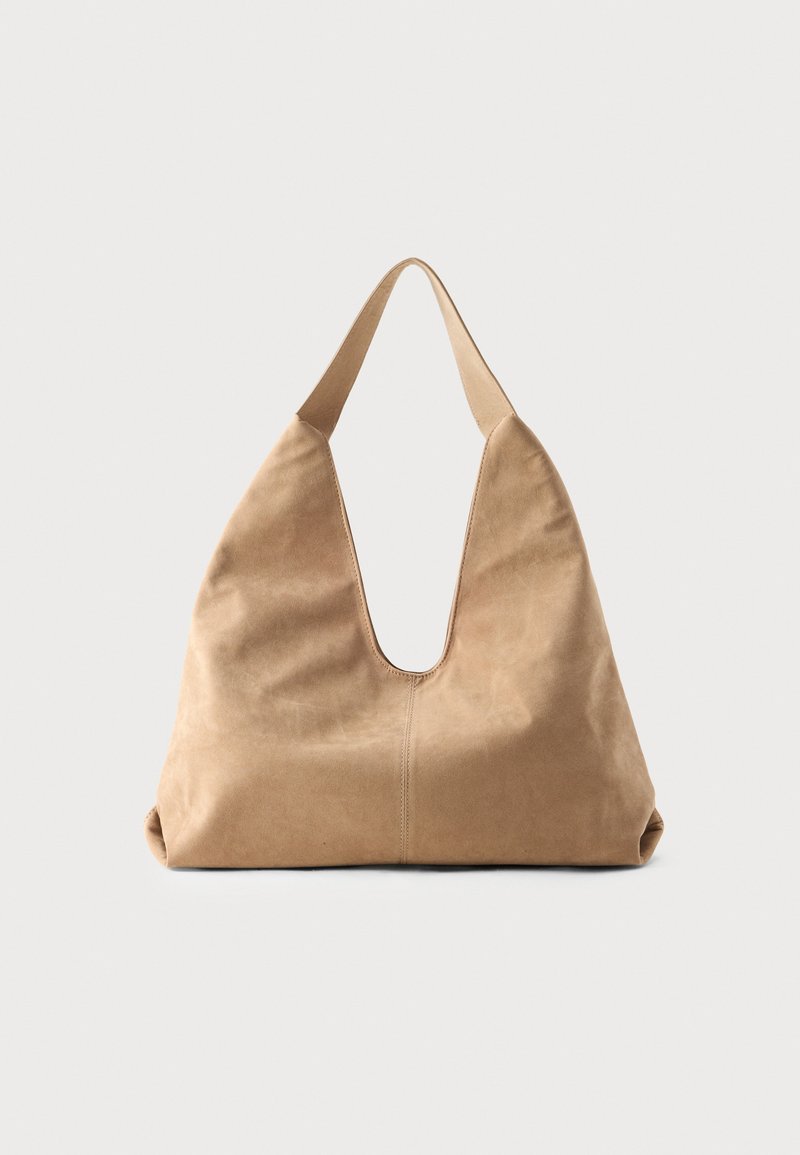 Hobo taske i blød beige ruskind med en dyb V-formet åbning, bred skulderrem og glat tekstur; har en afrundet bund for stabilitet.
