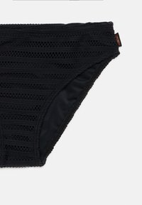 Črne bikini hlačke z reliefnim vzorcem, ki ima vodoravne črte in odprte tkanine kot poudarke. Robovi so zaključeni z kontrastnim obrobljanjem.