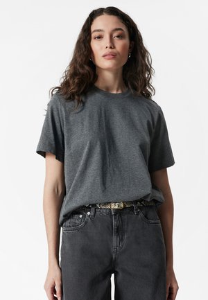 Gray cotton t-shirt with short sleeves, crew neckline, featuring a relaxed fit. Worn with black jeans and a patterned belt.