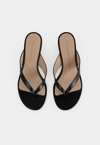 Sandales strings pour femmes en cuir noir avec semelles intérieures beiges, semelles plates et marquage Stuart Weitzman à l'intérieur.