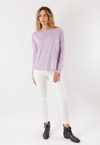 Top a maniche lunghe di un delicato color lavanda con una vestibilità comoda, abbinato a jeans bianchi e stivali neri alla caviglia. Tessuto morbido, design casual.