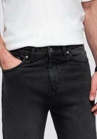 Mustat denim-farkut, joissa on tiukka muotoilu, etutaskut, hopeiset yksityiskohdat ja sileä pinta. Yhdistetty valkoiseen t-paitaan.