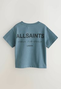 Petrolinsininen college-pikeepaita, jossa on lyhyet hihat. Selässä suurikokoiset mustat tekstit: "ALLSAINTS", japanilaisia merkkejä ja "LONDON".