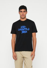 Juodas marškinėliai su mėlynu grafiniu tekstu „Karl Lagerfeld Jeans“. Pagaminti iš medvilnės, su trumpomis rankovėmis ir apvalia iškirpte.