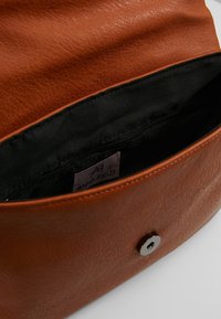 Brun läderhandväska inuti som visar en mjuk textur; svart foder med ett dragkedjefack; silverfärgad tryckknappsslutdetalj; etikett synlig.