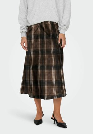Femme portant une jupe midi à carreaux marron associée à des talons slingback noirs et un haut à manches longues gris clair.