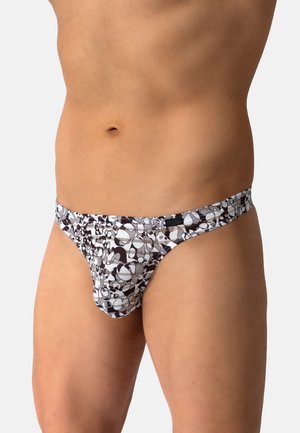Männlicher Torso mit schwarz-weiß gemusterten, tief sitzenden Bikinihosen vor einem schlichten hellen Hintergrund.