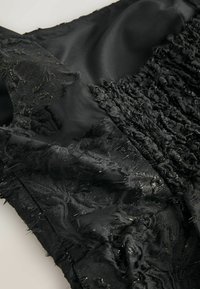 Must mustriga kangas, millel on tekstureeritud, kulunud osa, segatuna sileda satiiniga. Mõlemad alad on läikivad, luues kontrasti materjalide ja mustri vahel.