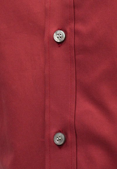 Crvena košulja na dugmad s glatkom, teksturiranom tkaninom. Ima srebrne dugmadi i kontrastno crvenu prošivenu liniju duž plavka.