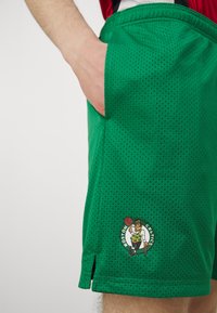 Roheline võrgust korvpallishorts, millel on küljekotid ja Boston Celticsi logo alumisel äärisel. Tekstuurne materjal ventilatsiooniga.