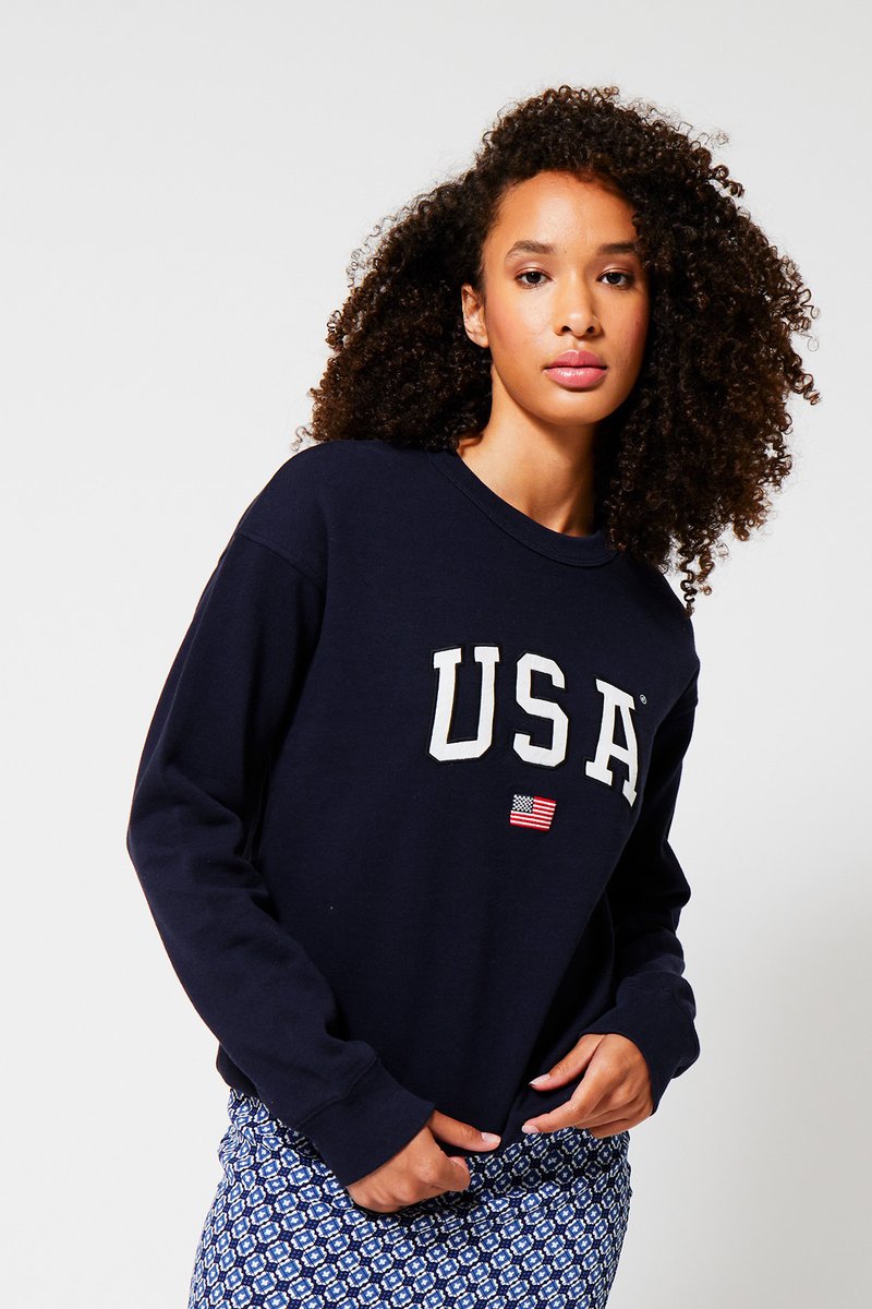 Navy blue sweatshirt featuring "USA" in white letters and a small American flag. Long sleeves with a relaxed fit, made of cotton material.