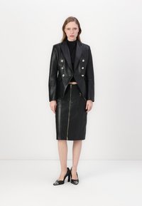 Svart skinn cropped blazer med sølvknapper, parret med en høyt liv svart skinn blyantkjole med glidelås foran. Svart hæler.