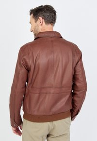 Braune Lederjacke mit Kragen, geripptem Saum und Rückennähten. Zeigt die Rückansicht und die strukturierte Oberfläche des Materials.