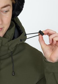 Groene waterdichte jas met een hoge kraag, voorzien van een zwarte trekkoord en verstelbare toggle. Zachte, met bont gevoerde capuchon en een gladde textuur.