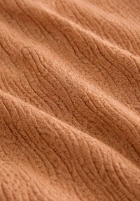 Tissu texturé de couleur terracotta chaude avec un motif froissé. Matériau doux, léger et légèrement extensible.