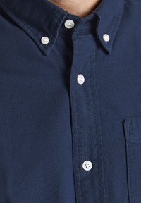 Camisa de botones azul marino hecha de tela texturada, con un cuello con costuras sutiles y botones de plástico blancos, incluyendo un bolsillo en el pecho.