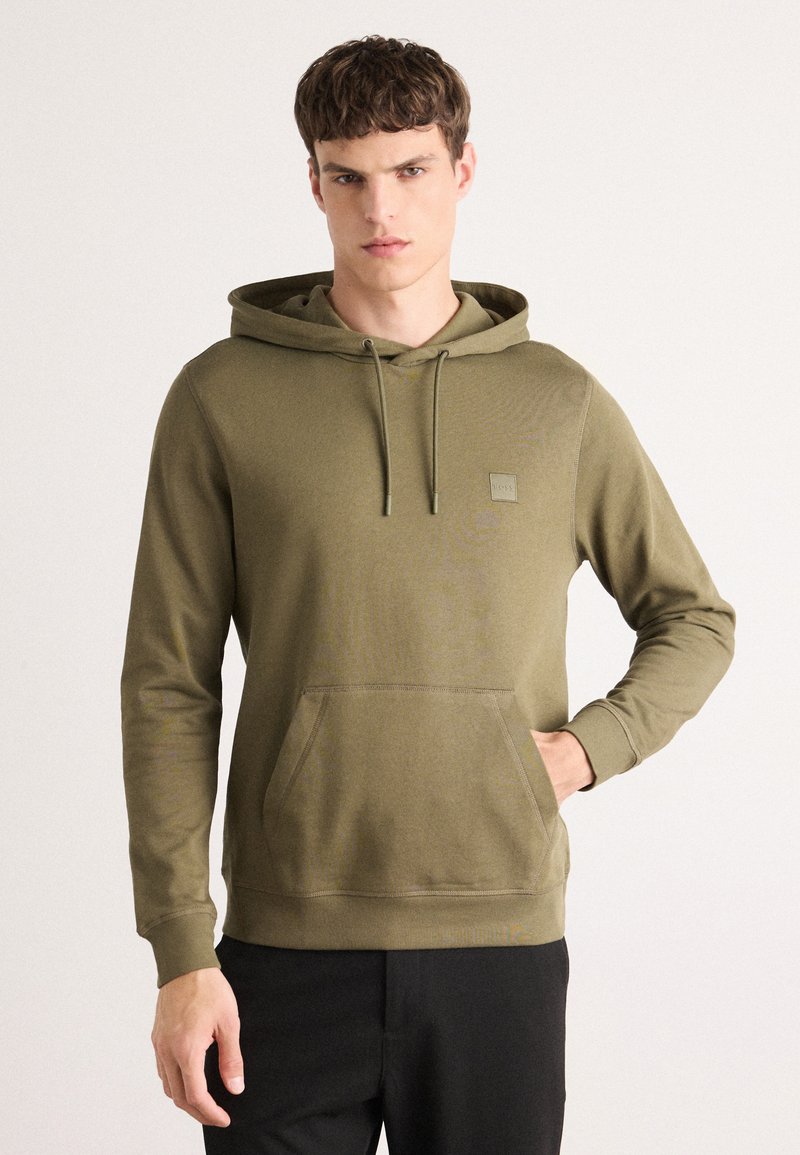 Olijfgroene hoodie met een trekkoord, kangoeroezak, ribgebreide manchetten en een klein logo-label op de borst. Zachte materiaalmix.