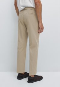 Beige skräddarsydda byxor med rak passform, med bakfickor och slät textur, kombinerade med mörka sneakers.