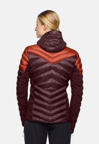 Giacca isolante color bordeaux con cappuccio, caratterizzata da pannelli di accento arancione e trapuntatura a zigzag. Realizzata in tessuto leggero e liscio con un design aderente.