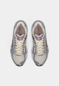 Ζευγάρι γκρι και λευκά αθλητικά παπούτσια Asics με εκρού κορδόνια και ροζ σήμανση, φωτογραφημένα από ψηλά σε απλό φόντο.