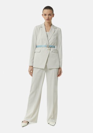 White tailored blazer with a light blue belt, paired with matching wide-leg trousers and pointed toe shoes. Smooth fabric and structured design.