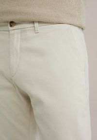 Light beige trousers with a textured fabric, featuring a button closure and side pockets. The material appears breathable and casual.