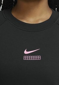 Svart sweatshirt med en rosa Nike-logotyp och ett rutmönster under. Tyget verkar mjukt med en ribbad krage.