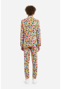 Abito colorato con un motivo di punti multicolori su uno sfondo chiaro; presenta un design su misura e pantaloni coordinati. Indossate sneakers bianche.