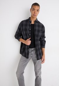 Svart och grå rutigt knapp-up skjorta, lättviktsmaterial, långärmad, oversize-passform, kombinerad med grå jeans och en svart linne.