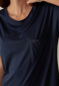 T-shirt a maniche corte blu navy realizzato in morbido cotone, con una piccola tasca sul petto sinistro e un colletto rotondo con cuciture semplici.