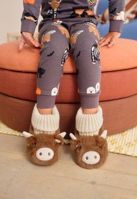 Chaussons marron à thème animalier avec une texture douce et pelucheuse, des bords-côtes crème et des oreilles et museau décoratifs, accompagnés d'un pyjama gris à motifs.